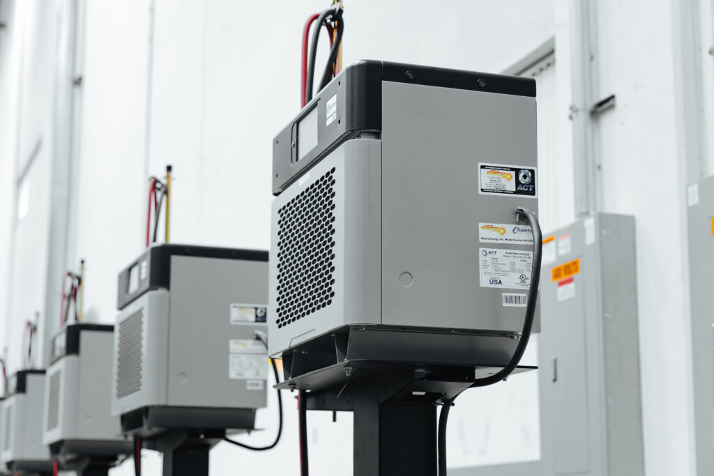 Row of gray industrial battery units on metal pedestals with vents and labels in a clean utility room